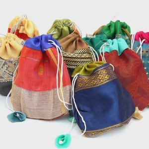 May include: A collection of small drawstring pouches made from various colorful fabrics, including red, blue, green, and yellow, featuring intricate woven patterns, metallic gold borders, and white cord closures, with the text Catfluff in the corner.