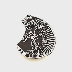 May include: A dark brown wooden printing block featuring a carved design of a curled cat. The cat is depicted in a sleeping position with its tail wrapped around its body, showcasing intricate white carved lines that define the feline form.