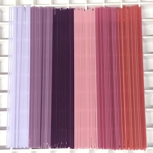 May include: A selection of thin, straight, plastic rods arranged vertically in a gradient of colours. The colour range includes shades of lavender, purple, pink, and red. The rods are evenly spaced and appear to be new.