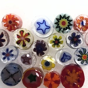 Pode incluir: Uma coleção de contas de vidro redondas com vários padrões millefiori coloridos. Cada conta exibe distintos desenhos florais, de estrelas ou geométricos em tons de vermelho, azul, amarelo, verde e preto incrustados em cilindros de vidro transparente.