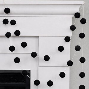 May include: A decorative garland featuring a series of solid black felt balls spaced evenly along a thin white string. The garland is draped in multiple loops, showcasing the uniform spherical shape and matte texture of each individual black ball.