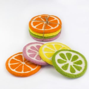 May include: A collection of colorful felt coasters shaped like citrus fruit slices. The coasters include orange, pink, yellow, and green designs, with white detailing. A stack of coasters is tied with twine.
