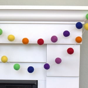 May include: A rainbow felt ball garland with purple, blue, green, yellow, orange, and red balls strung on a white string.