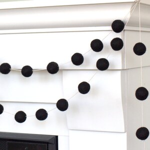 May include: A decorative garland featuring a series of solid black felt balls strung together on a thin white cord. The round, textured spheres are evenly spaced along the string, creating a simple, uniform design that hangs in two distinct loops.