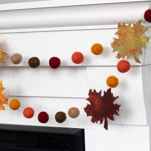 May include: A fall-themed garland with felt balls in shades of orange, red, brown, and tan, and felt leaves in shades of orange, brown, and yellow.