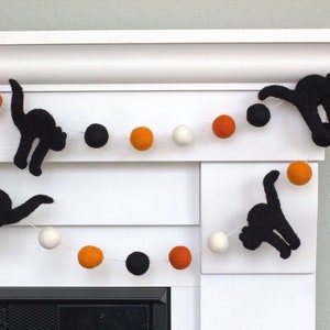 May include: A Halloween garland with black felt cat silhouettes and orange, white, and black pom-poms.