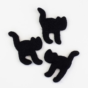 May include: Three black felt cat-shaped appliques, each depicted in a silhouette form with an arched back and a raised tail. These small, flat fabric pieces feature a soft, fuzzy texture and are arranged in a scattered pattern against a plain background.