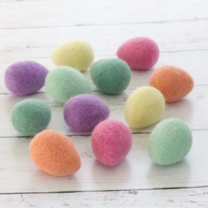 May include: A collection of colorful, felt Easter eggs in shades of purple, green, pink, orange, and yellow. The eggs are arranged on a white wooden surface, creating a cheerful and festive display. These decorative eggs are perfect for Easter.