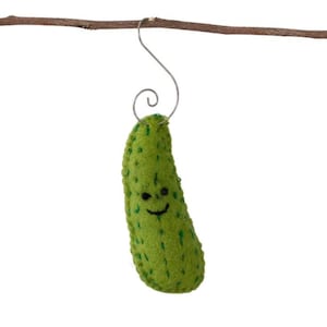 May include: A green felt pickle ornament with a smiling face and a wire hook for hanging. The pickle has a textured surface and is suspended from a small branch. A whimsical, handmade decoration.