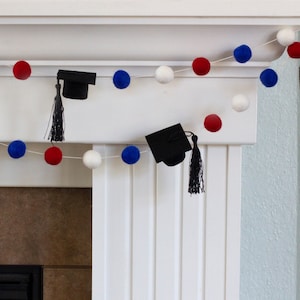 May include: A graduation garland with red, white, and blue pom-poms and black graduation caps with tassels.