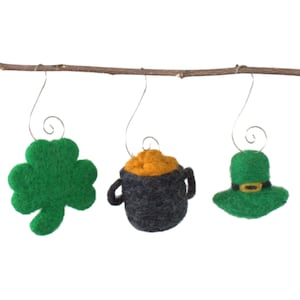 May include: Three felt ornaments hanging from a branch. The ornaments are a green shamrock, a pot of gold, and a green leprechaun hat.