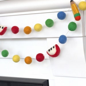 May include: A colorful felt garland with red apples, yellow pencils, and multi-colored pom-poms. This garland is perfect for a classroom or a child's room.