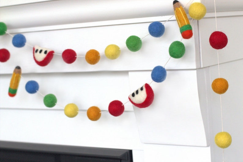 May include: A colorful felt garland with red apples, yellow pencils, and multi-colored pom-poms. This garland is perfect for a classroom or a child's room.