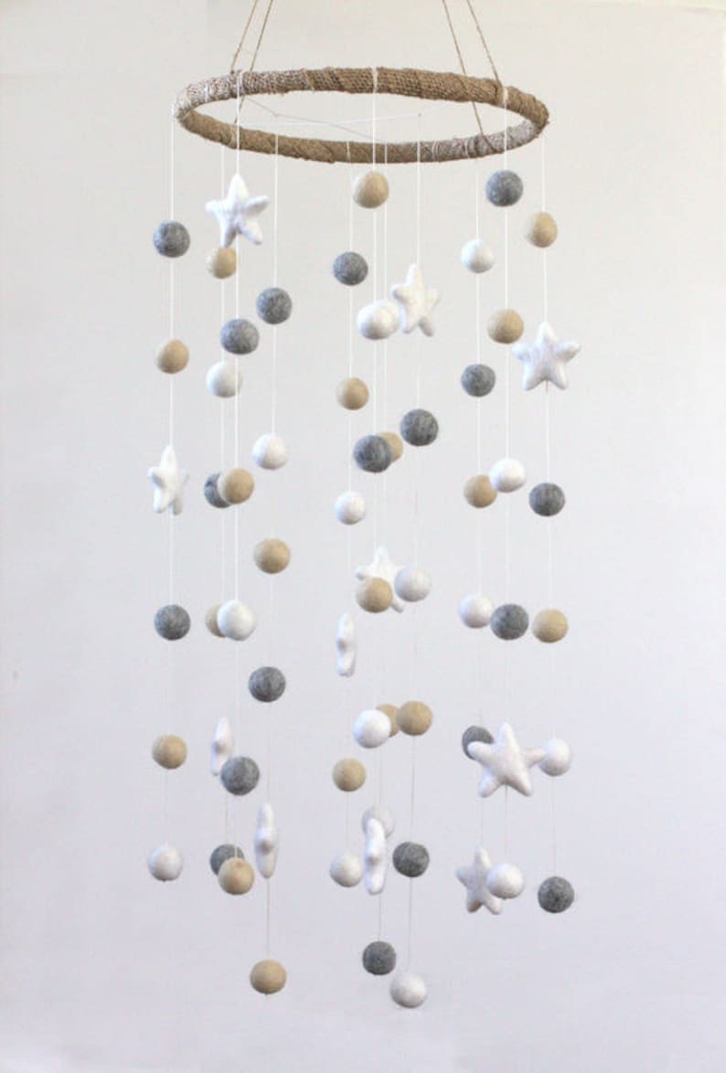 May include: A white, gray, and beige felt baby mobile with stars and balls hanging from a natural jute rope circle.