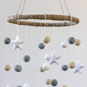 May include: A white, gray, and beige felt baby mobile with a natural jute ring. The mobile features felt stars and balls hanging from the ring.