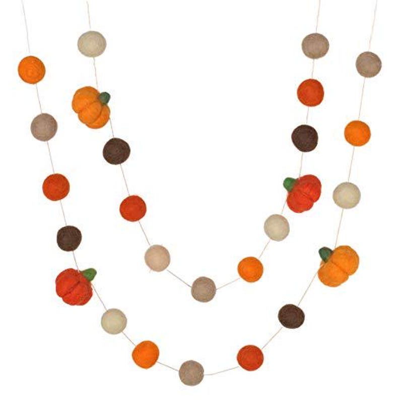 May include: A decorative garland featuring a series of felted wool balls in shades of orange, brown, and cream, interspersed with small, three-dimensional felt pumpkins that have green stems, all strung together on a thin, light-colored string.