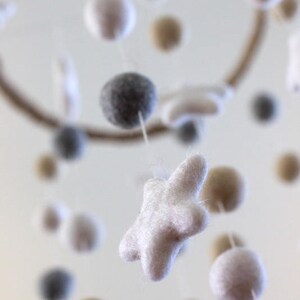 May include: A white felt star hangs from a mobile with other felt balls in gray, white, and beige.