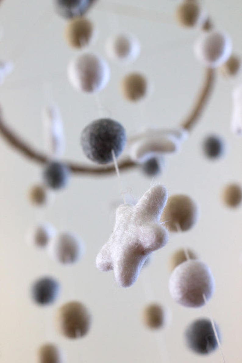 May include: A white felt star hangs from a mobile with other felt balls in gray, white, and beige.