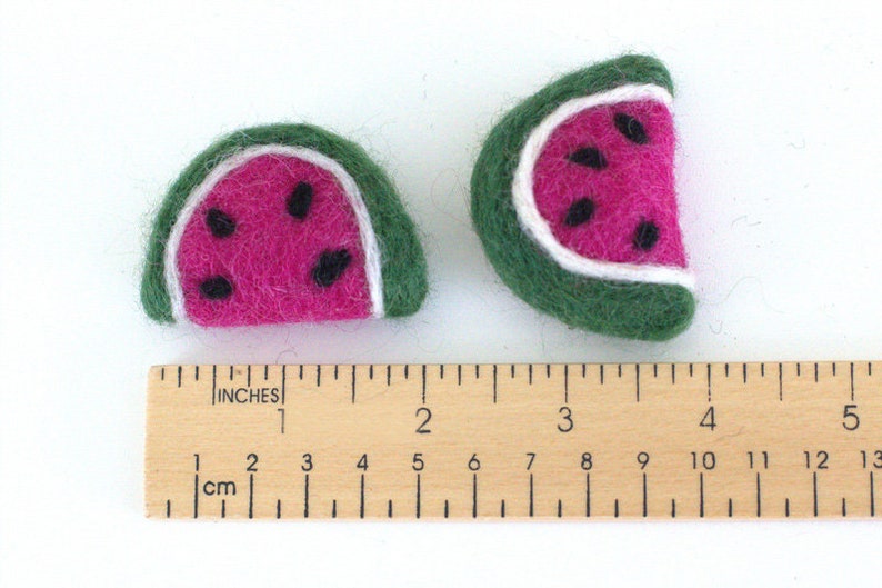 May include: Two felt watermelon slices, one larger than the other, with green rinds, white seeds, and pink flesh. The slices are measured against a wooden ruler.