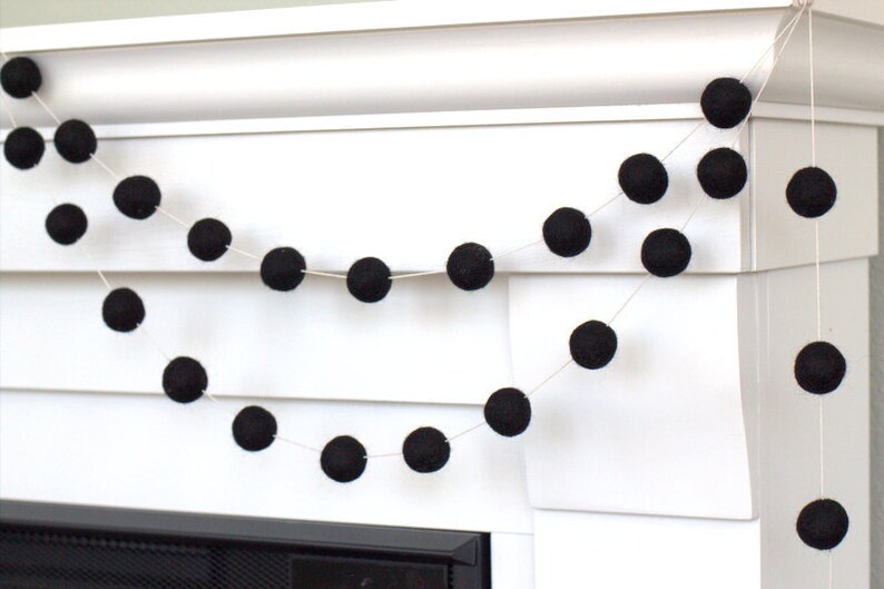 May include: A decorative garland featuring a series of solid black felt balls strung together on a thin white cord. The round, textured spheres are evenly spaced along the string, creating a simple, uniform design that hangs in two distinct loops.