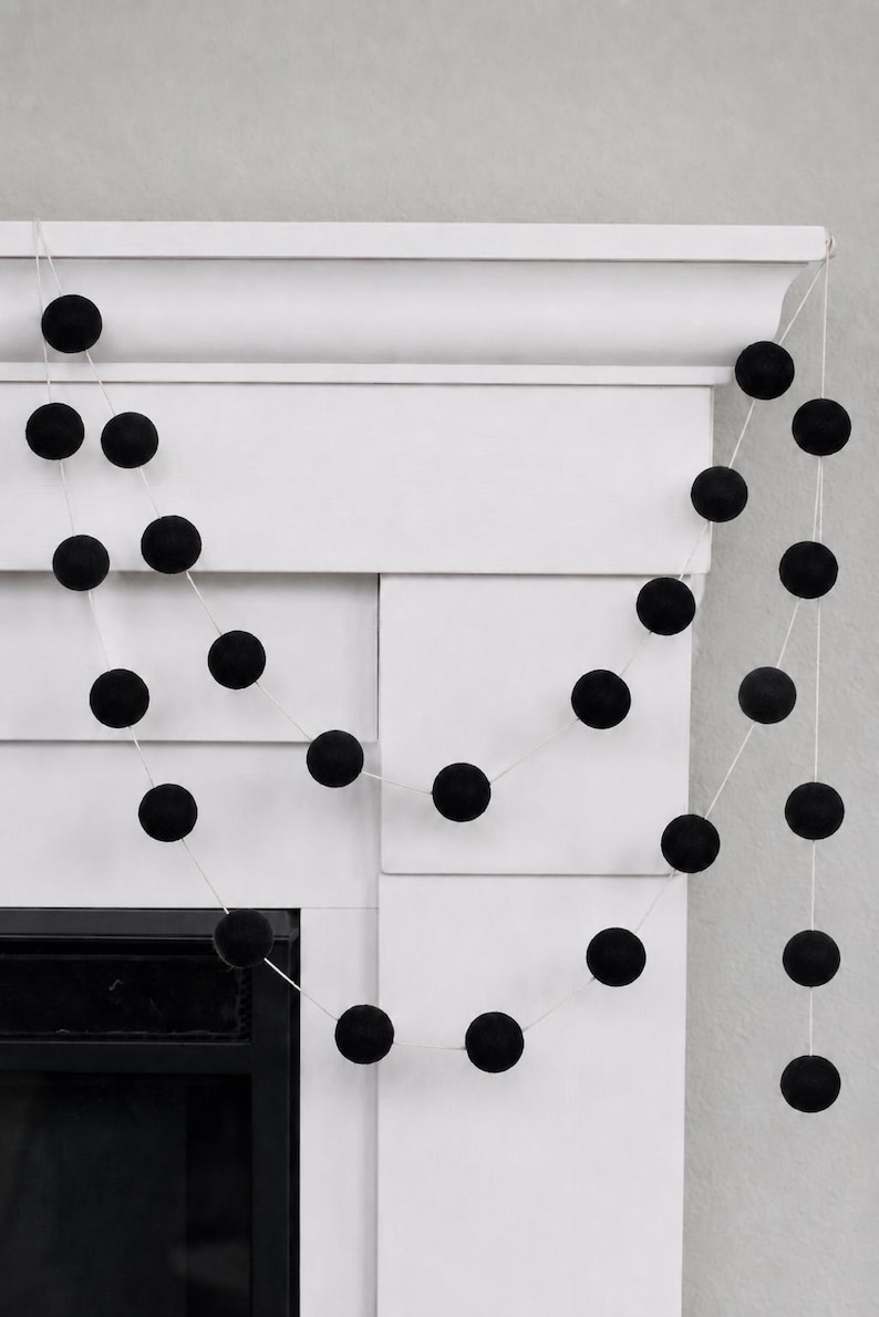 May include: A decorative garland featuring a series of solid black felt balls spaced evenly along a thin white string. The garland is draped in multiple loops, showcasing the uniform spherical shape and matte texture of each individual black ball.