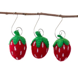 May include: Three felt strawberry ornaments hanging from a branch. Each ornament is red with white seeds and a green stem and leaves.