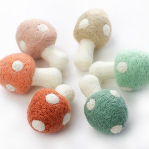 May include: Six felt mushroom ornaments in various colors, including pink, orange, green, and beige. Each mushroom has white polka dots and a white stem.