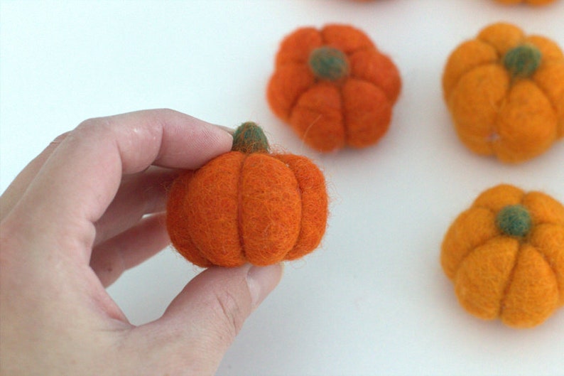 May include: Five felt pumpkins in orange and yellow with green stems. The pumpkins are small and round, and they are perfect for autumn decorations.