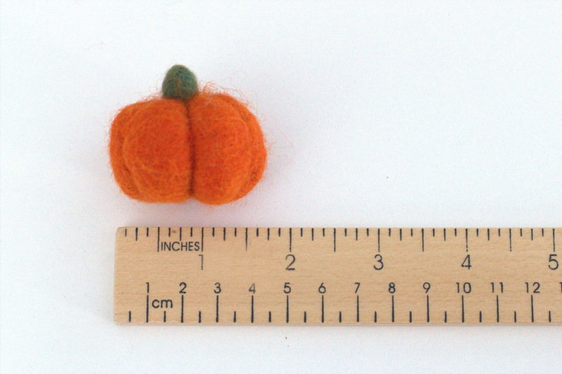 May include: A small, orange felt pumpkin with a green stem. The pumpkin is approximately 2.5 cm in diameter.