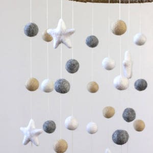 May include: A white, gray, and beige felt baby mobile with stars and balls hanging from a natural jute ring.