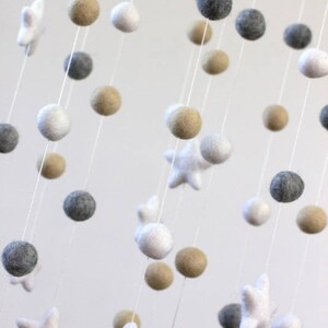 May include: A white, gray, and beige felt baby mobile with stars and pom-poms hanging from a white string.