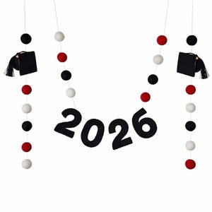 May include: A graduation-themed banner with the year "2026" in black felt letters. The banner is adorned with black graduation caps and strings of red, white, and black felt balls, creating a festive and celebratory decoration.