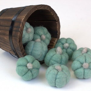 May include: A wooden barrel overflowing with teal felt pumpkins. The pumpkins are handmade and have a slightly textured surface.