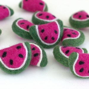 May include: A collection of felt watermelon slices in various sizes. The watermelon slices are green on the outside, white in the middle, and pink on the inside. The watermelon slices have black seeds.
