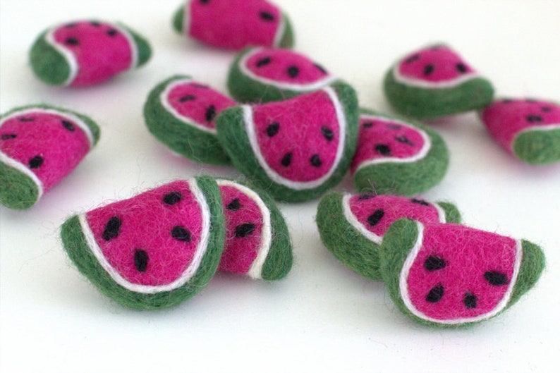 May include: A collection of felt watermelon slices in various sizes. The watermelon slices are green on the outside, white in the middle, and pink on the inside. The watermelon slices have black seeds.