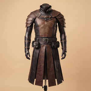K&ouml;nnte beinhalten: Ein R&uuml;stungsset aus braunem und schwarzem Leder mit geschichteten Schulterst&uuml;cken, einer Brustplatte mit Schnallenriemen, Armschienen, einem H&uuml;ftg&uuml;rtel mit zwei befestigten Taschen und einem langen, mehrteiligen Rock, der bis zu den Knien reicht.