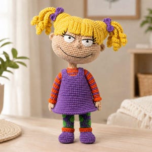 Peut inclure: Poupée au crochet faite à la main représentant un personnage de dessin animé avec des cheveux jaunes coiffés en couettes avec des nœuds violets. La poupée porte une robe violette sur un haut rayé orange et rouge, un pantalon à motifs verts et violets et des chaussures violettes.