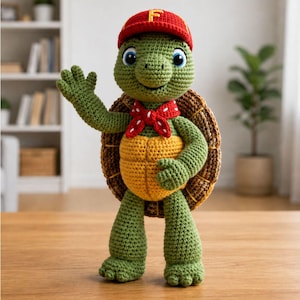 Peut inclure: Une poupée tortue en crochet avec une peau verte, un ventre jaune et une carapace brune. La tortue porte une casquette de baseball rouge avec une lettre F jaune sur le devant et un foulard rouge à pois blancs. La figurine a de grands yeux bleus.