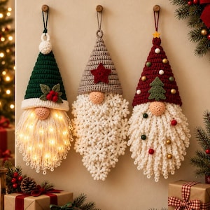 Peut inclure: Trois décorations suspendues en crochet en forme de gnomes avec des chapeaux pointus. Le gnome de gauche a un chapeau vert avec du houx, celui du centre un chapeau gris avec une étoile rouge, et celui de droite un chapeau rouge avec un sapin.