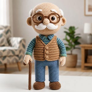 Puede incluir: Una muñeca de ganchillo de una persona mayor con cabeza beige, bigote blanco y gafas marrones. La muñeca viste una camisa azul de manga larga con estampado, un chaleco marrón abotonado y pantalones azules. Tiene zapatos marrones y un bastón.