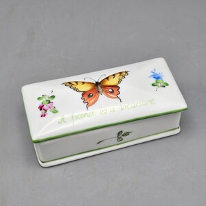 May include: A rectangular white ceramic trinket box featuring a hand-painted orange and yellow butterfly on the lid. The text A friend is a treasure is written in green script. Small floral accents in pink and blue decorate the lid.