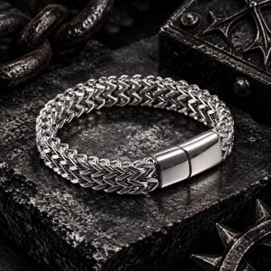 Pode incluir: Uma pulseira de metal prateado com um design de corrente de trigo densamente entrelaçada. A pulseira é construída com um fecho magnético retangular e liso que prende as duas extremidades da corrente, criando um elo contínuo e polido.