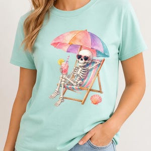 Może przedstawiać: Jasnozielony t-shirt w kolorze miętowym z grafiką szkieletu w okularach przeciwsłonecznych w kształcie serc, odpoczywającego na pasiastym leżaku pod kolorowym parasolem, trzymającego r&oacute;żowy nap&oacute;j z plasterkiem cytryny i muszelką.