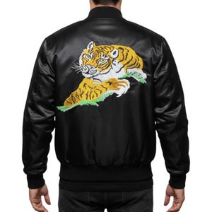 May include: Black satin bomber jacket with a large embroidered tiger design on the back. The tiger is yellow, orange, and white, with green accents. The jacket has a ribbed collar, cuffs, and hem.