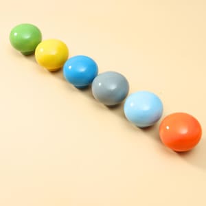 May include: A set of six spherical cabinet knobs arranged in a diagonal line. The knobs feature a smooth, glossy finish in distinct solid colors including lime green, bright yellow, royal blue, slate gray, sky blue, and vibrant orange.
