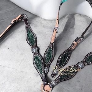 Peut inclure: Un collier de chasse pour cheval en cuir marron avec des incrustations de cristaux vert foncé, des ferrures en métal argenté et des accents de cristaux circulaires. Les lanières en cuir ont des boucles réglables et le texte Equi Luxe Horsewear est visible.