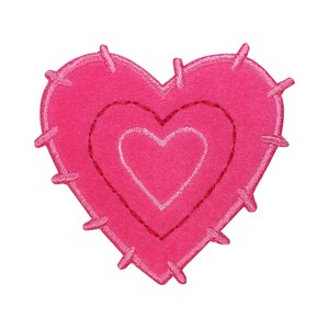 Può includere: Un cuore di feltro rosa con un cuore rosa più piccolo all'interno, entrambi con un contorno bianco. I bordi del cuore sono cuciti con una linea irregolare e frastagliata.