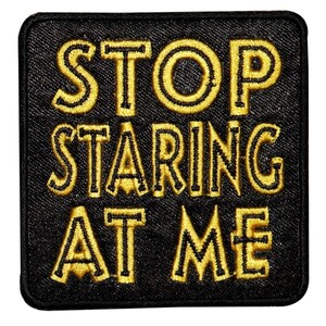 May include: Black fabric patch with yellow embroidered text that reads "STOP STARING AT ME".