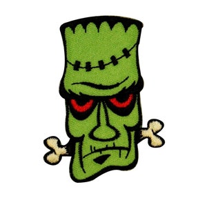 May include: Green Frankenstein monster face with red eyes and a bone sticking out of his mouth. The monster is stitched up on the forehead.
