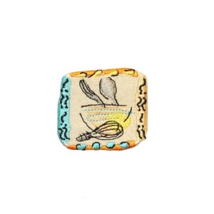 May include: Embroidered patch featuring a bowl with a spoon and whisk. The patch has a beige background with a yellow and blue bowl design. The border is orange, teal, and black. A kitchen-themed accessory.